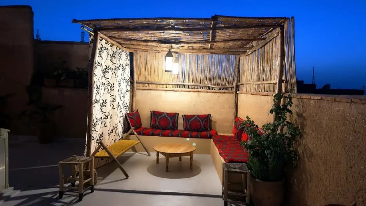Rooftop de Dar Mobylette à la tombée de la nuit : banquette aux coussins rouges, lanternes allumées et ciel bleu nuit