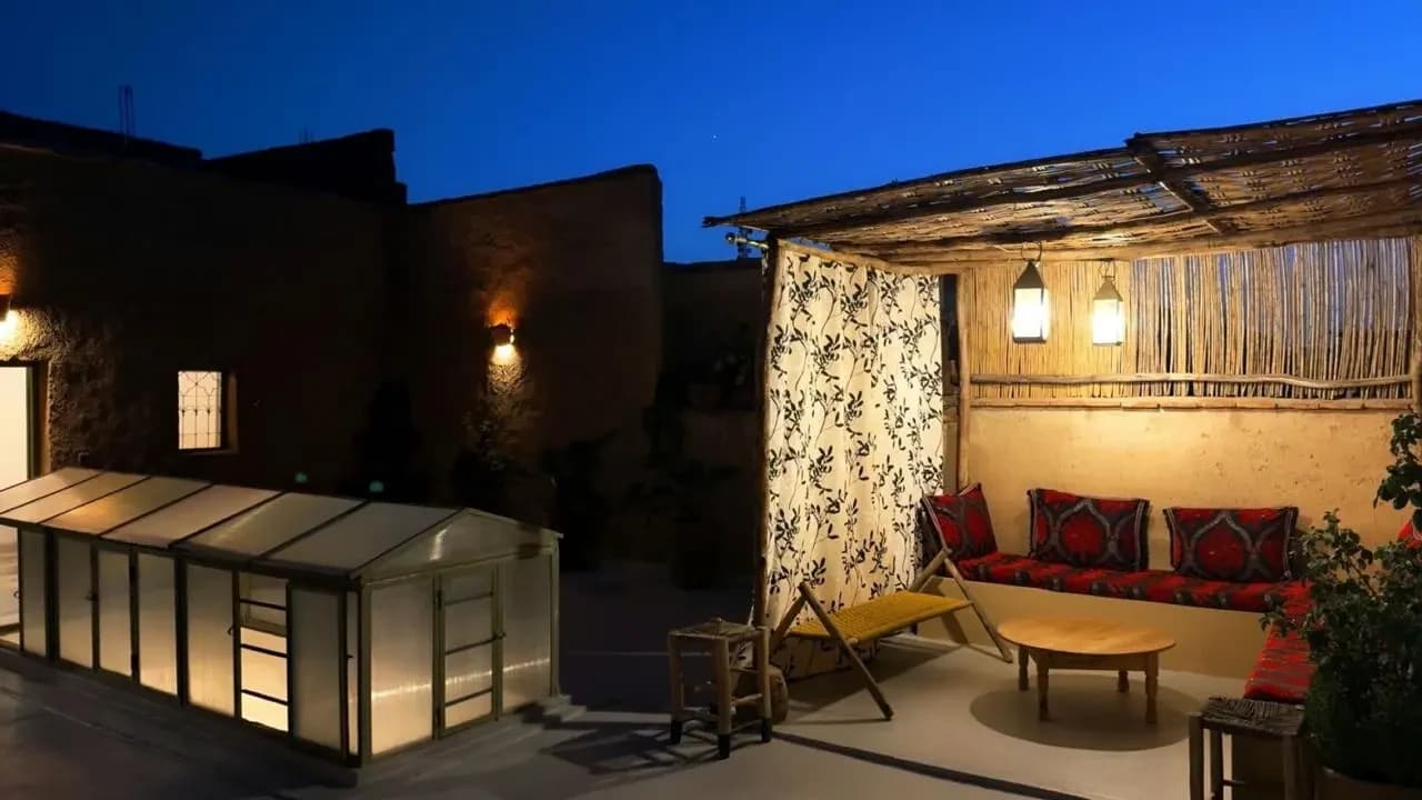 Terrasse sur le toit le soir, lanternes allumées, banquette et plantes sous un ciel bleu intense
